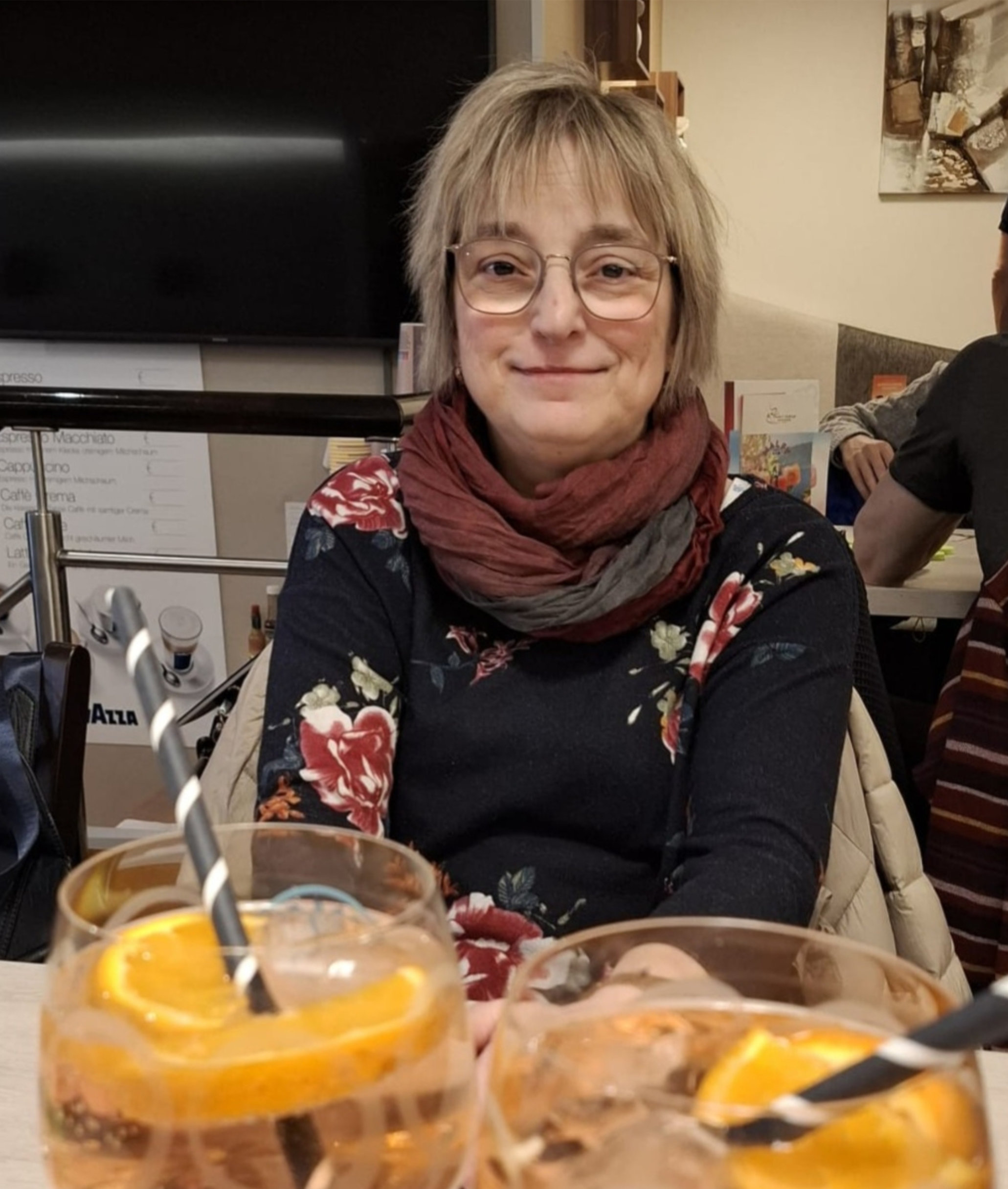 60plus Babette Frau mit Brille und Schal im Café.