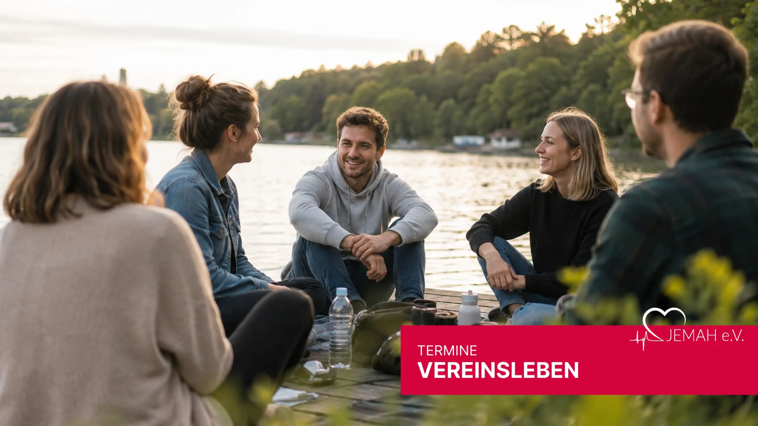 Fünf junge Erwachsene sitzen lächelnd auf einem Steg am See, umgeben von Natur. Im Vordergrund: jemah e.V. Logo.